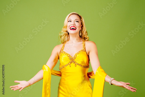 Fotografie, Tablou Enjoying the limelight, an elegant blonde with arms out, isolated on green studi