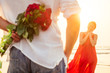 happy beautiful woman in red dress receiving a gift from a man by sea sunset.surprise wife from husband bouquet of roses women's day March 8 and Valentine's Day.engagement love at first sight romantic