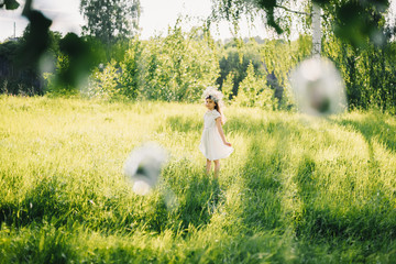 girl in a white dress with a wreath on her head on a meadow in nature on a Sunny summer day