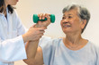 Senior elderly Asia woman with medical caregiver or physical therapist helping patient holding dumbbell in physical therapy session. Healthy old people concept.