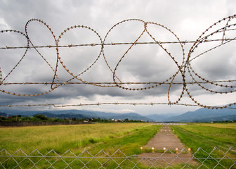 Fence from a barbed wire against the background of a runway of the airport and mountains