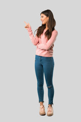 Full body of Teenager girl with pink shirt pointing finger to the side in lateral position on isolated grey background