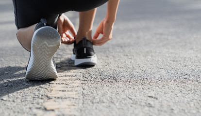 Wall Mural - A young woman stopped to tie a string while running in the stadium, Fitness woman runner tying shoelace before running 