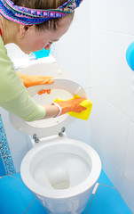 Wall Mural - Woman in orange rubber gloves cleaning toilet with pink cloth