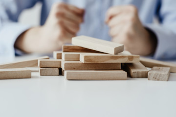 Wall Mural - Scattered wooden blocks on the table in the background sitting man dressed in a business shirt. Concept of disorder, lack of order. Problems with the organization of time and work.