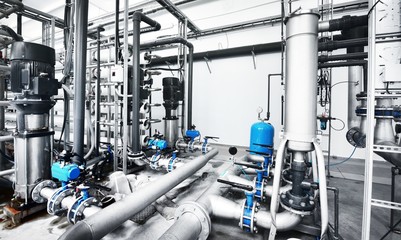 Large industrial water treatment and boiler room. Shiny steel metal pipes and blue pumps and valves.