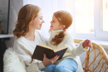 happy family mother reads book to child to daughter by window