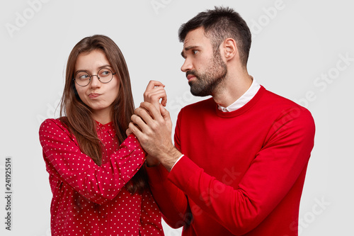 Fotografía Desperate young Caucasian man holds hand of girlfriend, looks with miserable expression, asks for forgiveness, feels guilty