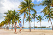 © Maridav - Miami people lifestyle - couple walking holding hands talking enjoying walk on beach with palm trees. Florida travel destination.