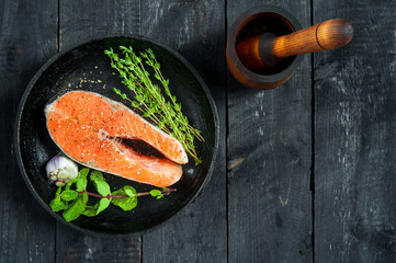 Raw red fish steak with herbs and garlic in a cast-iron pan. Top view. Copy space.