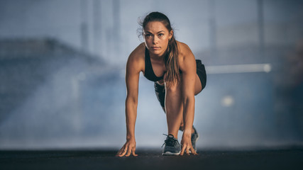 Wall Mural - Beautiful Strong Fitness Girl in Black Athletic Top and Shorts Ready for Start Sprint. She is in an Urban Environment Under a Bridge with Foggy Background.