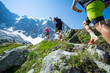 Three trail runners running up a steep trail towards the mountains in the Alps
