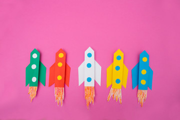 top view of flying multi-colored rockets from paper on a pink background