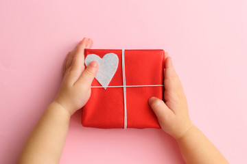 Child hands holding beautiful gift box on pink background. Holiday, bright and festive view, flat lay. Valentines day greeting banner. Father day, Mother day or Birthday celebration.