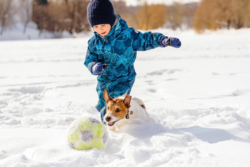 4 years old boy playing football (soccer) with his dog on snow