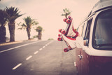 Pair of woman feet with roller blades vintage style over the window of legendary camper van - long road and tropical palms and light in background - freedom and rock'n roll lifestyle pin-up concept