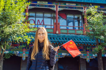 Wall Mural - Enjoying vacation in China. Young woman with national chinese flag on the background of the old Chinese street. Travel to China concept. Visa free transit 72 hours, 144 hours in China