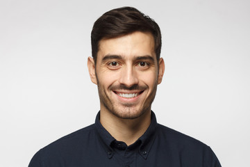 Closeup headshot of business man standing against gray background, smiling with satisfaction and confidence