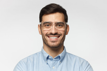 Wall Mural - Smart businessman smiling at camera, wearing trendy transparent glasses, isolated on gray background