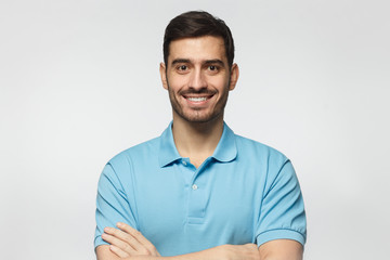 Wall Mural - Portrait of smiling handsome man in blue polo shirt, standing with crossed arms isolated on grey background