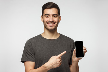 Portrait of happy man demonstrating blank smartphone and pointing to empty screen with smile. Copyspace for yor app