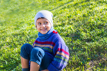 Wall Mural - cheerful boy in a hat and sweater sitting on the grass