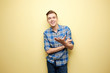 © Leika production - Affable  guy dressed in a plaid shirt and jeans is standing on a yellow background in the studio
