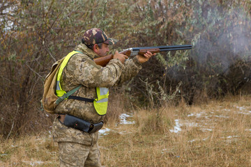 Wall Mural - Hunter with a gun and a dog go on the first snow in the steppe, Hunting pheasant in a reflective vest	