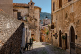 Fototapeta Dmuchawce - A narrow  traditional street paved with stone among stone houses in a medieval small town Sermoneta not far from Rome. Hills covered with green forest are visible in the background.