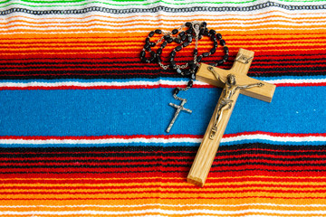 A crucifix and rosary beads on a colorful Mexican sarape.