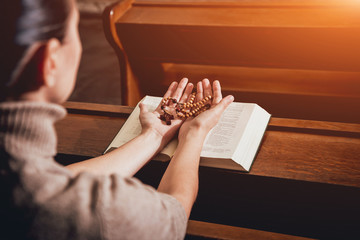 Wall Mural - Christian woman praying in church. Hands crossed and Holy Bible on wooden desk.