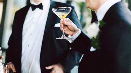 men in tuxedos holding a martini glass at a wedding party