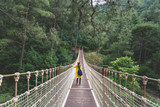 Fototapeta Mosty linowy / wiszący - Woman with raincoat standing on suspension bridge.