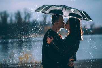 young couple standing under a dark umbrella