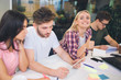 © estradaanton - Picture of cheerful young blonde woman look on camer and smile. Other students work on their projects at table. They are serious and concentrated.
