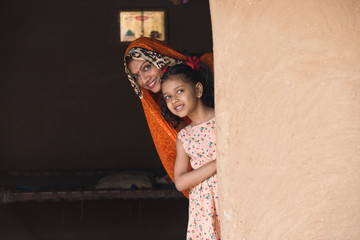 Wall Mural - Happy mother and daughter peeking from rural house