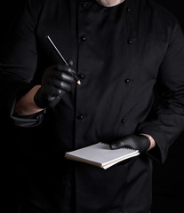 Wall Mural - chef in black uniform and gloves is holding a blank notebook