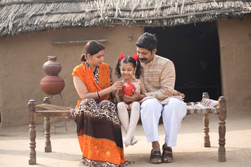 Wall Mural - Happy indian family holding piggy bank at village