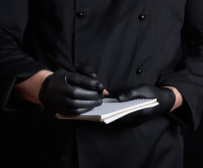 Wall Mural - chef in black uniform and latex gloves holding a blank notebook and a black wooden pencil