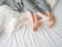 Close Up Of Male And Female Feet On A Bed - Loving Couple Under Grey Blanket In The Bedroom - Concept Of Sensual And Intimate Moment Of Lovers.