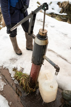 A Man Pours Water With A Water Pump Into A Plastic Canister, On A Winter Evening, In The Village.
