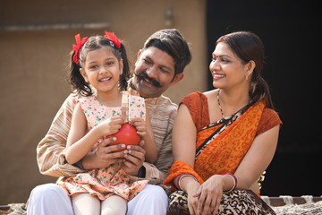 Wall Mural - Indian family holding piggy bank at home