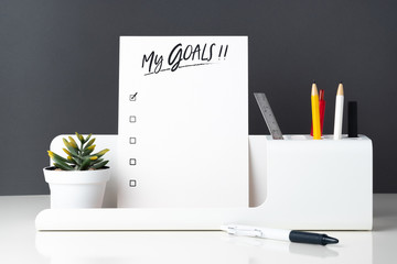 Poster - My goals list on notepad at modern office stationery on white table and dark grey wall.pencil, notepad,ruler,pen and pencil box with plant.