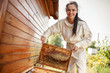 Young female beekeeper pulls out from the hive a wooden frame with honeycomb. Collect honey. Beekeeping concept