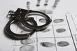 Police handcuffs and criminal fingerprints card, closeup