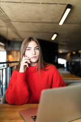 Young woman talk on phone and working on laptop in a cafe.