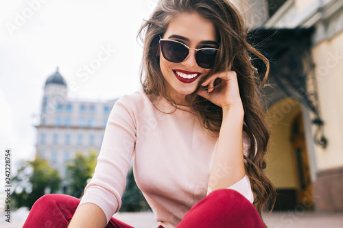 Cuadros en Lienzo Buttom view of attractive girl in sunglasses with snow-white smile, long hairstyle and vinous lips chilling in city