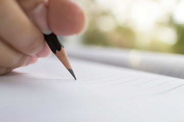 Close-up hand holding a black pencil, Female hand writing with a pencil on a white paper in the morning with morning sunlight.