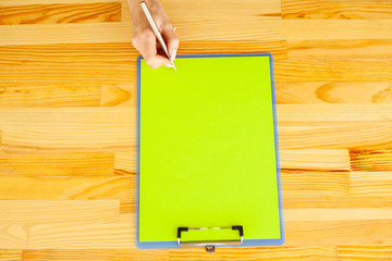 Office Hand Holding a Folder with a Green Color Paper and Pen on the Background of the Wooden Table. Copyspace. Place for Text