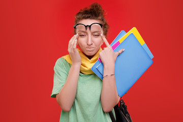 Visually impaired young girl student pulling the corners of her eyes holding a folder for study on a red background. Woman is tired of long computer work in the office